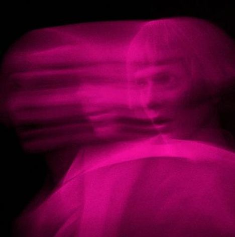 Kein Text vorhanden. Verschwommene, mehrfach überlagerte Darstellung eines Gesichts in pinkem Licht.