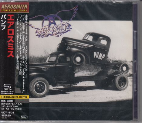 Links ragt ein roter Balken mit japanischem Text hoch. Oben steht "AEROSMITH". Zwei alte Lastwagen sind übereinander gestapelt.