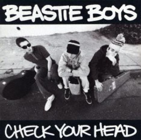 "BEASTIE BOYS" oben, "CHECK YOUR HEAD" unten. Schwarz-weiß Foto von drei sitzenden Personen auf Gehweg mit Instrumentenkoffern.