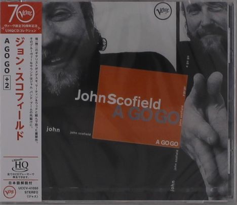Text links: "ジョン・スコフィールド A GO GO +2". In der Mitte "John Scofield A GO GO". Schwarz-weißes Foto eines Mannes als Hintergrund.