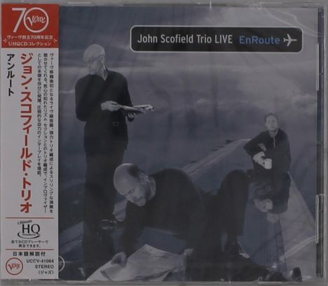 "John Scofield Trio LIVE EnRoute" steht auf einem dunklen Cover. Drei Männer in Schwarz auf einem Flugzeugflügel.