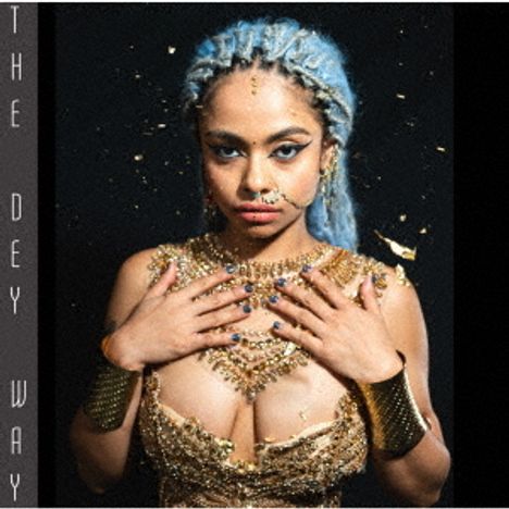 Text: "THE DEY WAY". Frau mit blauem Haar, goldenen Verzierungen und eindrucksvollem Schmuck.