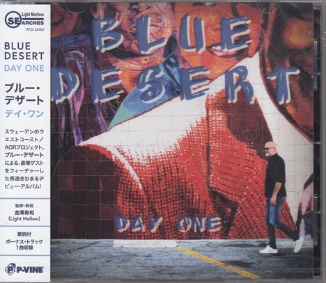Text: "BLUE DESERT DAY ONE". Mann steht vor einer bunten Wandmalerei. Links japanische Schriftzeichen.
