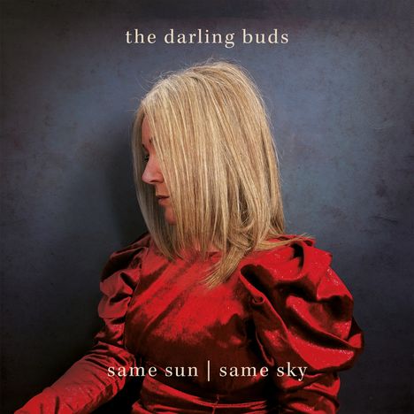 Text: "the darling buds", "same sun | same sky". Frau im roten Kleid vor dunklem Hintergrund.