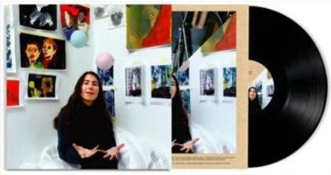 Ein schwarzes Vinyl neben einem Albumcover. Eine Frau sitzt vor bunten Gemälden und jongliert mit Bällen.