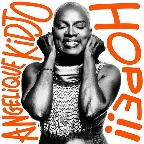 ANGELIQUE KIDJO, HOPE!! Eine Frau lächelt mit geschlossenen Augen und hält sich die Hände an die Ohren.