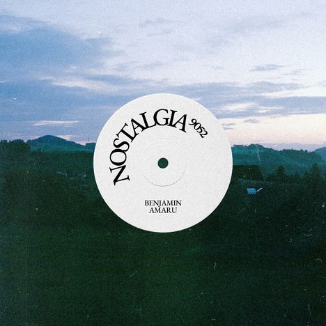 Text in runder Form: "NOSTALGIA 9052", darunter "BENJAMIN AMARU". Hintergrund zeigt eine Landschaft bei Sonnenuntergang.