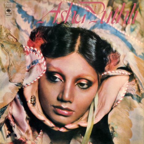 "Asha Puthli" steht oben in rosa Schrift. Frau mit kunstvoll geschminktem Gesicht, elegant drapiertem Schal und nachdenklichem Blick.