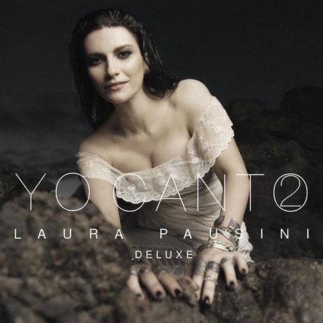 „YO CANTO“, „LAURA PAUSINI“, „DELUXE“. Eine Frau in weißem Kleid, kniet auf Felsen, mit dunklem Hintergrund.