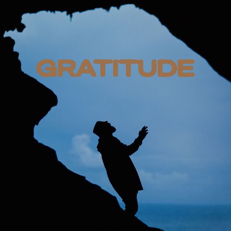 Text "GRATITUDE" vor einem blauen Himmel; Silhouette einer Person in einer Höhle.