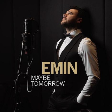 Text: "EMIN MAYBE TOMORROW". Ein Mann in formeller Kleidung lehnt an eine Wand neben einem Mikrofon.