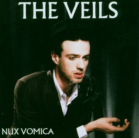 "The Veils", "Nux Vomica". Ein Mann in Anzug und Hut mit nachdenklichem Blick, hält seine Hände offen.