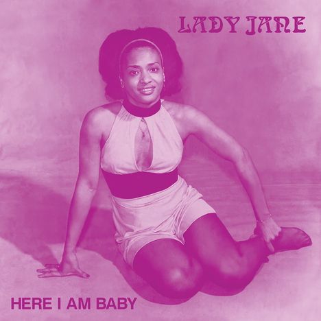 Text: "LADY JANE" oben und "HERE I AM BABY" unten. Eine Frau in einem ärmellosen Outfit sitzt auf dem Boden.