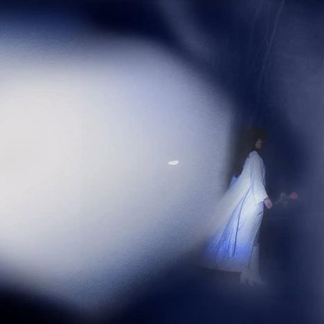 Unschärfe mit blauer und weißer Lichtkomposition; ein Mensch in weißem Gewand am Rand sichtbar.