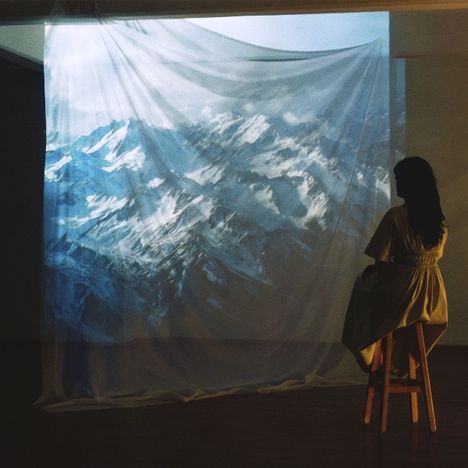 Ein Leinwand-Projekt zeigt verschneite Berge; eine Person sitzt auf einem Hocker und betrachtet die Projektion.