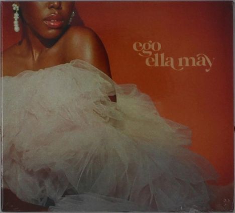 Text: "ego ella may". Frau in weißem Tüllkleid, Perlenohrringe, vor orangenem Hintergrund.