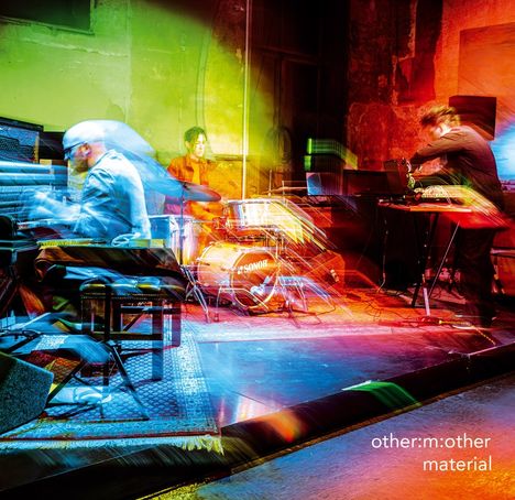 Text: "other:m:other material". Eine farbenfrohe Live-Performance mit Trommel, Keyboards und elektronischen Geräten.