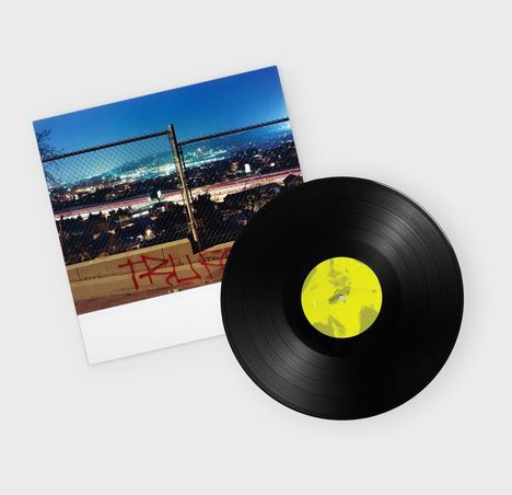 Ein Vinyl mit gelbem Etikett liegt auf einem Cover mit Stadtansicht bei Nacht, Gitterzaun und Graffiti.