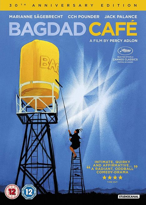 "Bagdad Café" 30th Anniversary Edition. Gelber Wasserturm, Person auf Leiter, blauer Himmel.