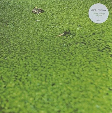 "ANTON PEARSON Driving Through Belgium" auf rundem weißem Aufkleber; grüner Teich mit Eulenauge sichtbar.