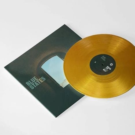 Text: "BLUE STATES." Goldene Vinylplatte halb auf einem dunkelgrünen Cover mit Fensterblick in den Himmel.