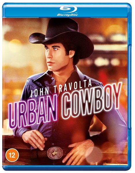„JOHN TRAVOLTA URBAN COWBOY“. Ein Mann im Cowboyhut und blauer Kleidung steht im Fokus.