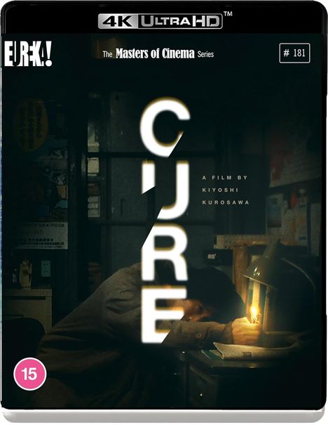 Text: "CURE", "A film by Kiyoshi Kurosawa". Dunkler Raum, Person schläft an einem Schreibtisch, beleuchtet von einer Schreibtischlampe.