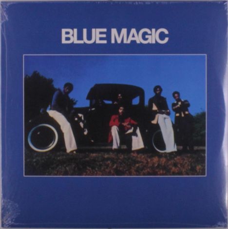 Text: "BLUE MAGIC". Eine Fotografie zeigt vier Personen neben einem Auto vor einem blauen Himmel.