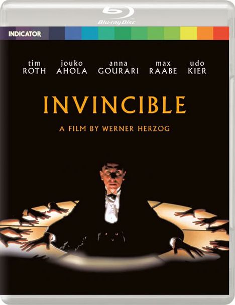 Oben stehen die Namen Tim Roth, Jouko Ahola, Anna Gourari, Max Raabe, Udo Kier. „INVINCIBLE“ ist mittig, darunter "A Film by Werner Herzog". Ein Mann im Anzug wird von vielen Händen umgeben, dramatisch beleuchtet.