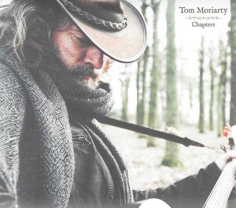 Text: "Tom Moriarty Chapters". Ein Mann mit Cowboyhut spielt Gitarre in einem Wald. Er trägt einen Schal.