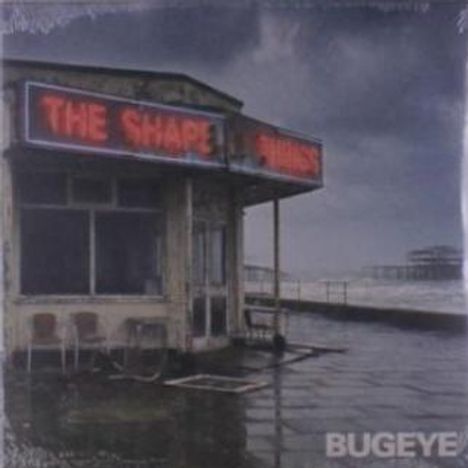 "THE SHAPE OF THINGS" leuchtet auf einem alten Gebäude am Meer. Dunkle Wolken und ein verlassenes Pier im Hintergrund.