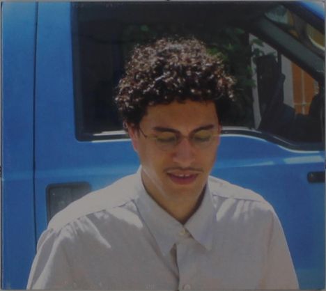 Ich kann keine Texte erkennen. Ein Mann mit Brille vor einem blauen Fahrzeug, trägt ein helles Hemd.