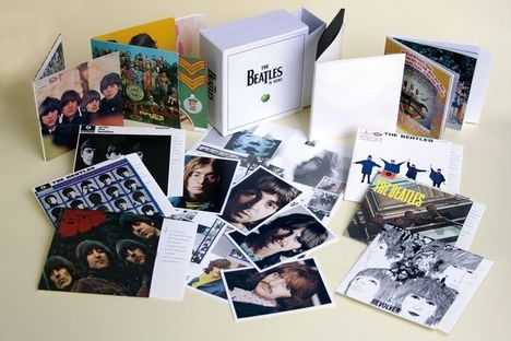 "The Beatles in Mono" auf einem Box-Set. Verschiedene Albumcover und Porträtfotos sind verstreut auf einem Tisch.
