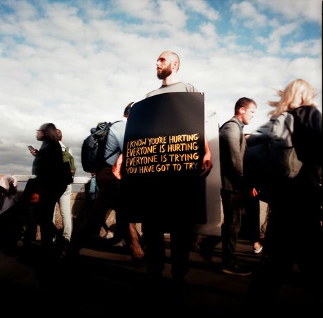 Ein Mann hält ein Schild: "I know you're hurting everyone is hurting everyone is trying you have got to try."