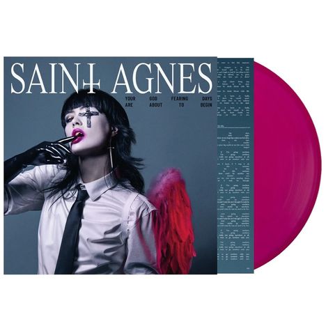 „SAINT AGNES“ in großen Buchstaben, Person mit auffälligem Make-up, schwarzem Handschuh und roten Engelsflügeln.