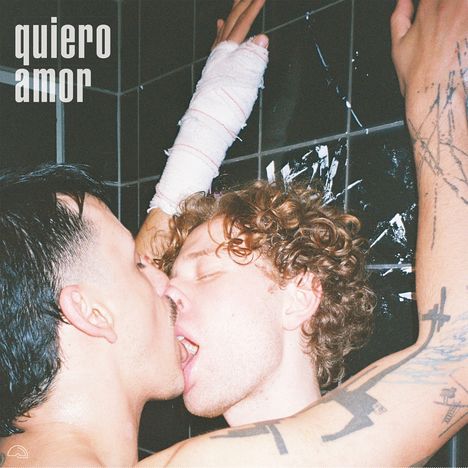 "quiero amor" steht oben links. Zwei Personen küssen sich leidenschaftlich in einer dunklen Umgebung. Eine hat einen Gipsarm.
