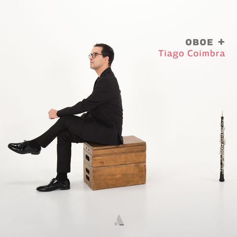 "OBEO + Tiago Coimbra" in schwarzen und roten Buchstaben links oben. Ein Mann im Anzug sitzt auf Holzkisten. Eine Oboe steht rechts.