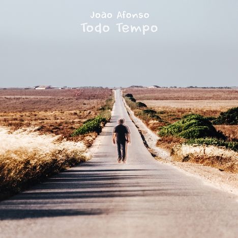 "João Afonso Todo Tempo" steht oben. Eine Person geht eine lange, gerade Straße entlang, umgeben von trockener Landschaft.