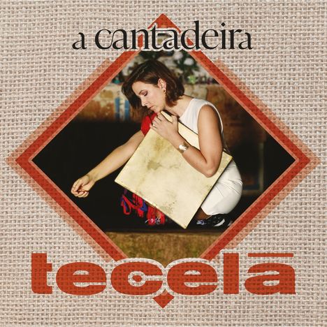 „a cantadeira“ und „tecelã“ sind auf einer stoffähnlichen Textur. Eine Frau in Weiß hält ein quadratisches Objekt.