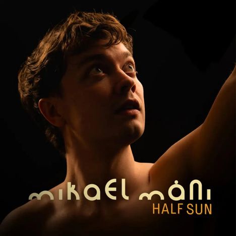 „Mikael Máni Half Sun“. Eine Person blickt aufmerksam nach oben, vor dunklem Hintergrund.