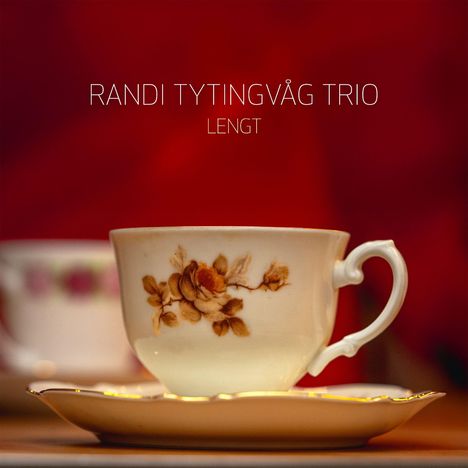 Text: "RANDI TYTINGVÅG TRIO LENGT". Eine verzierte Teetasse vor einem roten Hintergrund.
