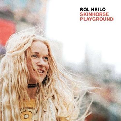 Text: "Sol Heilo Skinhorse Playground." Eine lächelnde Frau mit langen blonden Haaren in unscharfer städtischer Umgebung.