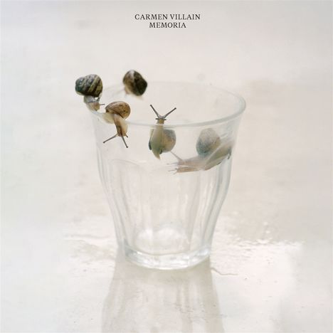 „CARMEN VILLAIN MEMORIA“ steht oben. Schnecken kriechen auf einem transparenten Glas in hellem Ambiente.