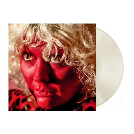 Ein Gesicht mit roter Haut, lockigem blondem Haar, gelben Augen und einem intensiven Blick. Eine Schallplatte ist sichtbar.