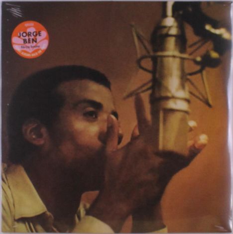 Roter Sticker: "JORGE BEN". Ein Mann singt konzentriert in ein Mikrofon. Dunkler Hintergrund.