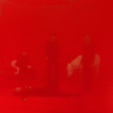 Rotes, verschwommenes Bild; schemenhaft erkennbare Menschen und ein weißes Pferd. Surreal und mystisch.