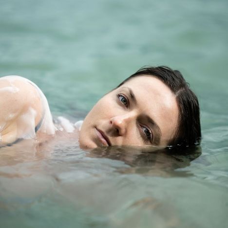 Eine Person mit nassem Haar liegt entspannt im Wasser, ihr Gesicht zeigt einen ruhigen Ausdruck.