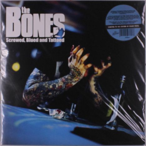 „The Bones, Screwed, Blued and Tattooed“. Tätowierte Person verdeckt Gesicht mit Händen, bläuliche Beleuchtung.