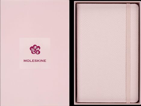 Moleskine und ein Blumenlogo auf einer rosa Schachtel, daneben ein rosa Notizbuch mit strukturierter Oberfläche.
