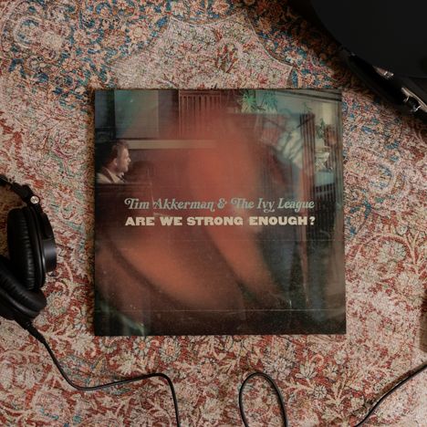 Schallplatten-Cover mit der Aufschrift „Tim Akkerman & The Ivy League - Are We Strong Enough?“, daneben Kopfhörer auf Teppich.